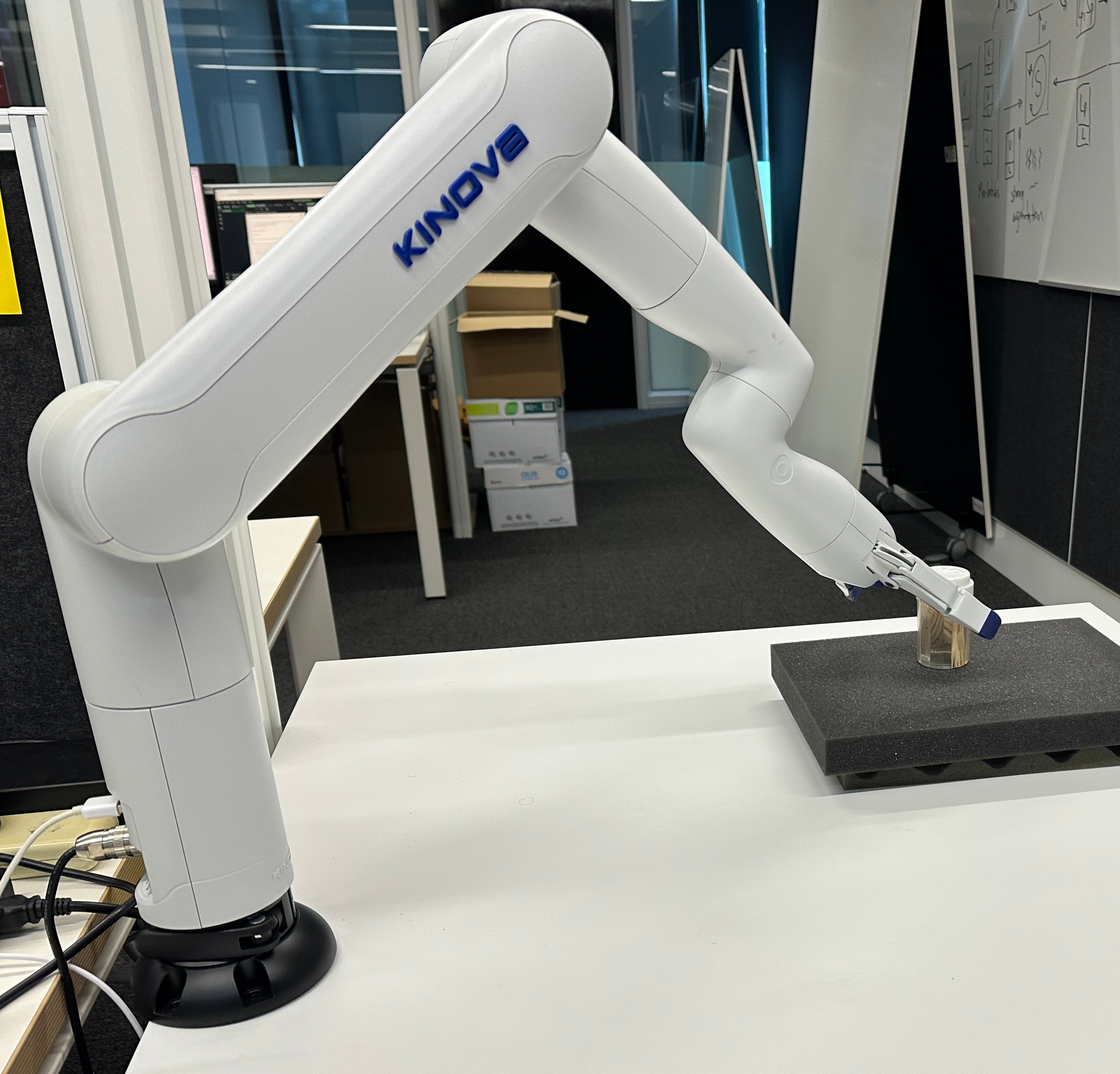 Physical Kinova robotic arm grasping an object on a table